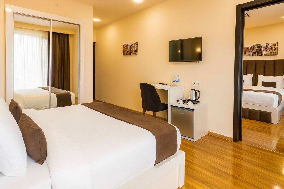 Habitación de hotel con dos camas, un escritorio con silla, televisión y una pequeña kitchenette.