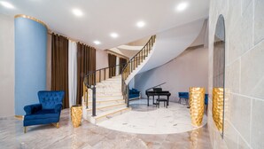 Un espacio habitable amplio con una imponente escalera, un sillón azul, un piano y un piso de mármol.