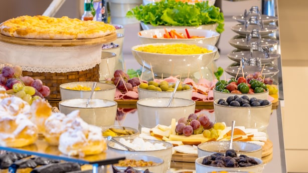 Un bufé con diversos alimentos, como ensaladas, quesos y postres.