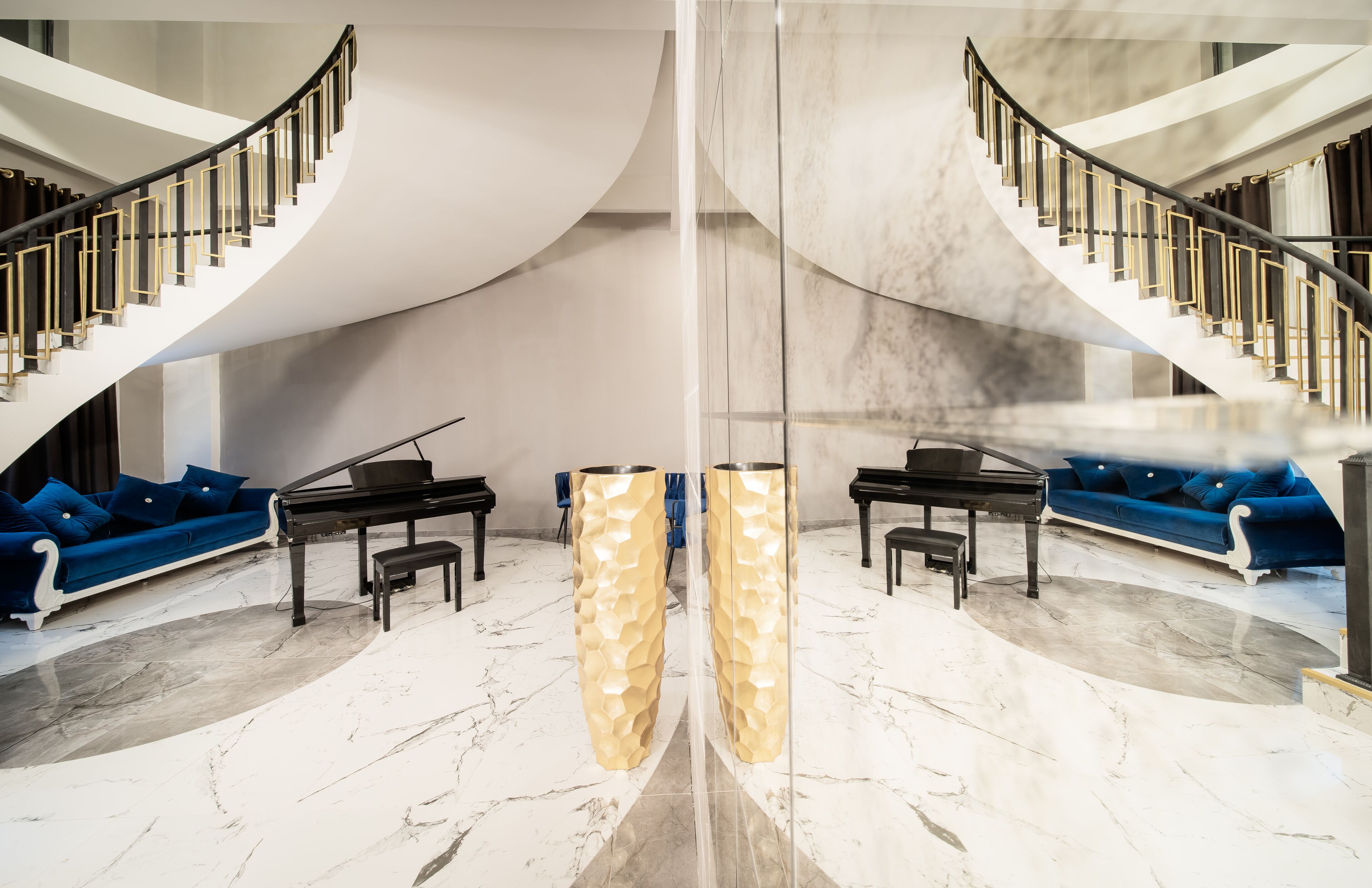 A grand lobby with a marble floor, a grand piano, a blue sofa, and a staircase with a glass barrier.