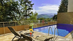 Un área junto a la piscina con sillones, una mesa con bebidas y vistas a montañas.
