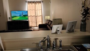 A kitchen with a sink, a television displaying a golf game, a laptop, and a tablet on a counter. - Chateau 18, spacious townhouse in Tickfaw, LA (Tickfaw)