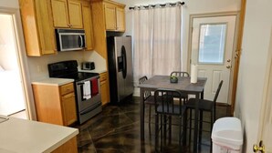 A compact kitchen with wooden cabinets, a microwave, a refrigerator, a stove, and a dining table with chairs. - Chateau 18, spacious townhouse in Tickfaw, LA (Tickfaw)