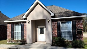A two-story building with a beige facade, a small entrance with a white door, and a brick exterior. - Chateau 18, spacious townhouse in Tickfaw, LA (Tickfaw)