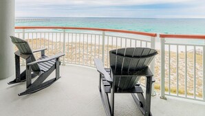 Un balcon avec deux fauteuils Adirondack et un fauteuil Adirondack noir, donnant sur une plage et l’océan.