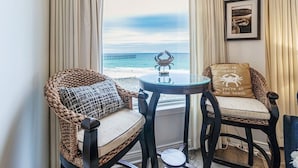 Une pièce avec vue sur l’océan, comprenant deux fauteuils en osier avec des coussins, une petite table ronde et un luminaire suspendu.