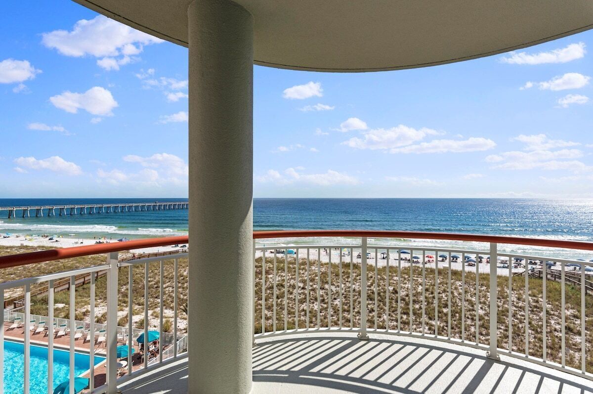 A balcony with a view of the beach, ocean, and a pier.