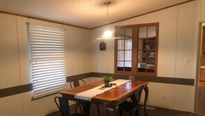 Une salle à manger avec une table en bois, quatre chaises, une plante en pot et une fenêtre avec des stores.