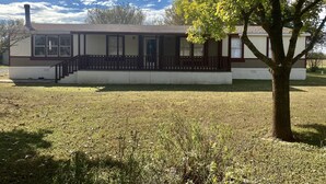 Une maison de plain-pied avec un porche à l’avant, une cheminée et un arbre dans le jardin.