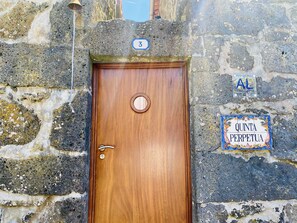 A wooden door with a round handle and a keyhole, set in a stone wall with a sign above reading "3" and another sign below stating "QUINTA PERPETUA". - Studio (Luz)