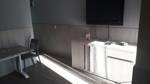 Een kleine kitchenette met een wit aanrecht, een stoel en een aan de muur bevestigde televisie.