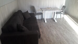 Een kamer met een donkerbruine bank, een kleine tafel met stoelen, en een houten vloer.