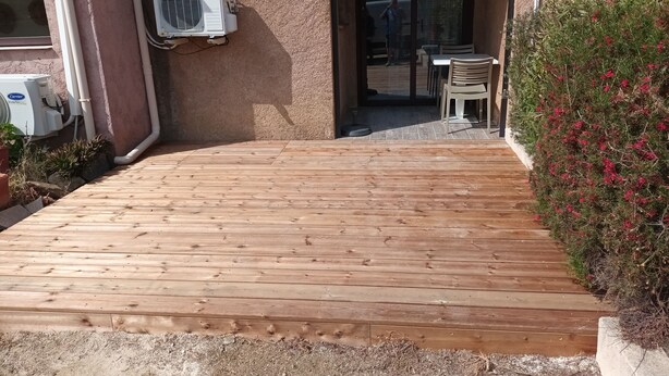 Een houten terras dat leidt naar een gebouw met buiten zitplaatsen.