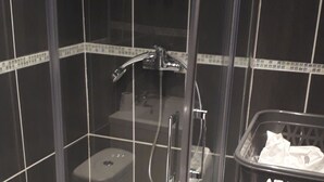 Een douchecabine met glazen wanden, een handdouche en een handmixer.