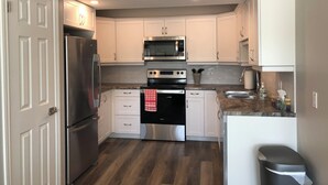 A compact kitchen with white cabinets, stainless steel appliances, and a wooden floor.