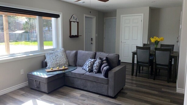 A living room with a grey sectional sofa, a small ottoman, and a dining table with chairs.