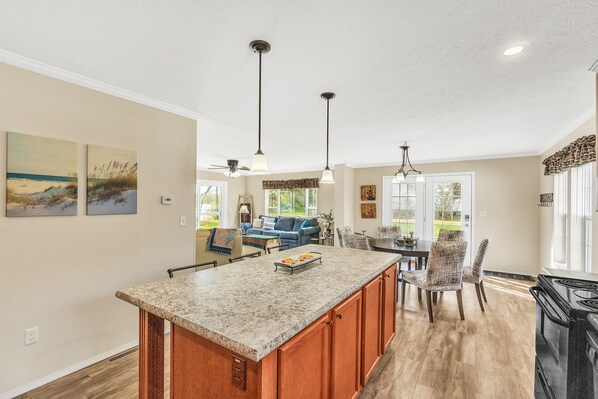 A spacious kitchen with a granite countertop, wooden cabinets, and a dining area with chairs and a table.