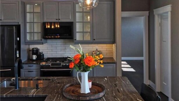 Una cocina moderna con una isla central, iluminación colgante y un jarrón con flores.
