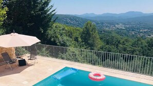 A swimming pool with a view of a mountainous landscape, a stone bench, and a lounge chair.
