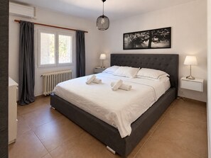 A neatly made bed with white linens and towels, a grey upholstered headboard, a wall-mounted picture of a tree, and a bedside table with a lamp. - SPACIOUS VILLA  MIMOZA  (Montauroux)