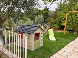 Un patio trasero cercado con casa de juegos, tobogán y columpio.