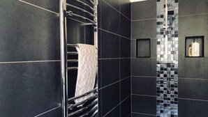 A modern bathroom with black tiles, a chrome towel rack, and a shower area with a mosaic tile design.