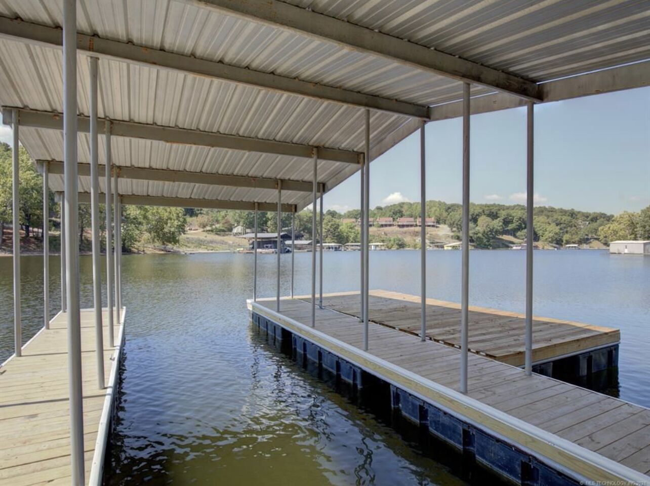 A covered dock extending into a calm lake, surrounded by trees and buildings.