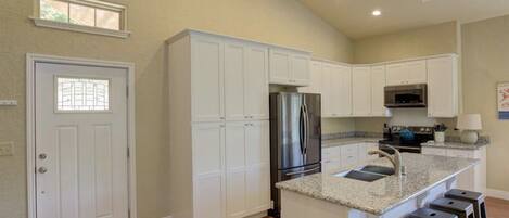 A kitchen with white cabinets, a stainless steel refrigerator, a microwave, and a granite countertop.