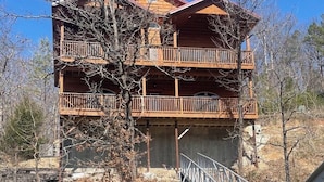 Une cabane en rondins à deux étages, dotée d’un balcon et située au bord d’un plan d’eau.