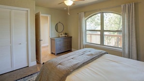 Une chambre à coucher comprenant un lit, une commode, un ventilateur de plafond, une fenêtre avec vue et une porte donnant sur une autre pièce.