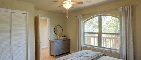Un dormitorio con cama, cómoda, ventilador de techo, ventana con vistas y puerta que da a otra habitación.