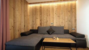 Ein modernes Wohnzimmer mit einer Eckcouch, einer Wand in Holzoptik und einem Couchtisch aus Holz.