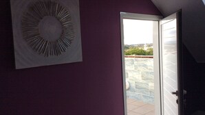 Porta aperta che dà su un balcone con vista su una piscina e edifici in lontananza.