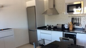 Una cucina compatta con frigorifero, microonde e fornello. C'è un tavolo da pranzo con sedie e una lavastoviglie.