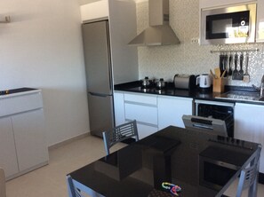 A compact kitchen with a refrigerator, microwave, and stove. There is a dining table with chairs and a dishwasher.