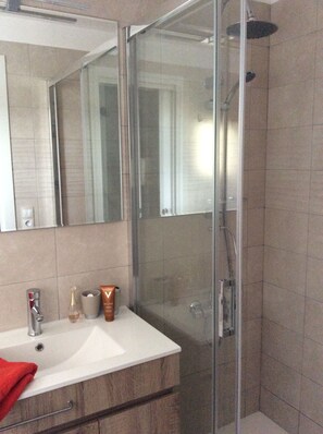 Une salle de bain moderne avec une douche à l’italienne en verre, un lavabo blanc et un grand miroir.