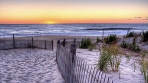 A beach with a wooden fence and sand dunes. - Coastal Charm- 4BR  Spacious, with Resort Pool- Bright and Inviting (Ocean View)