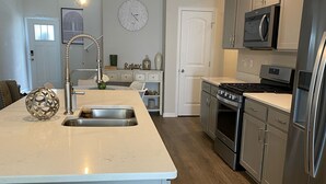 A kitchen with a central island, stainless steel appliances, and a clock on the wall. - Coastal Charm- 4BR  Spacious, with Resort Pool- Bright and Inviting (Ocean View)