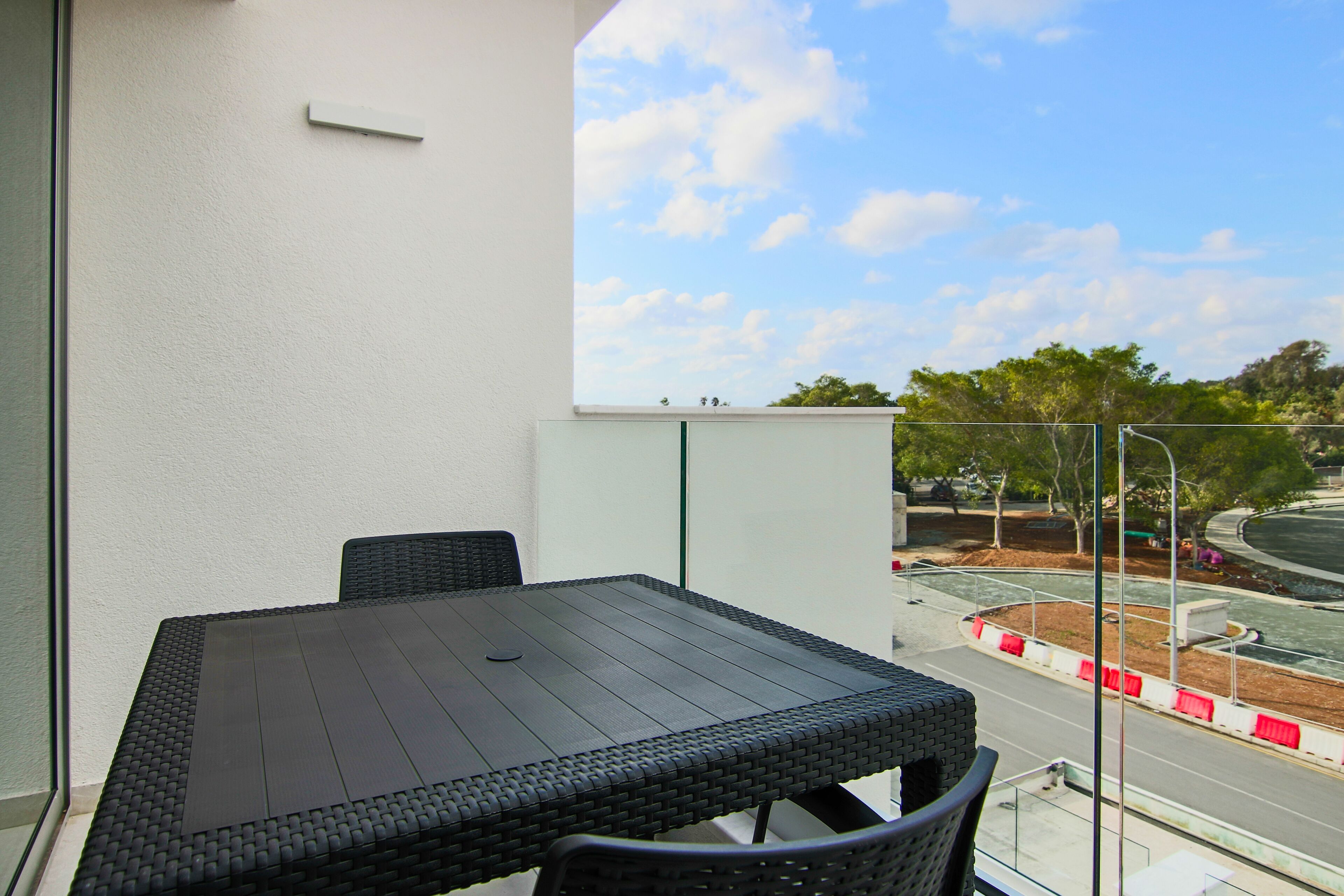 A balcony with a table and chairs, a view of the street, and a clear sky.