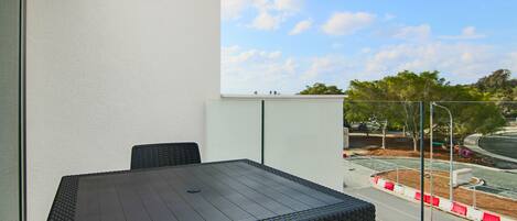 A balcony with a table and chairs, a view of the street, and a clear sky.