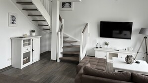 Een moderne woonkamer met een trap, een flatscreen televisie, een bank en een bureau met een lamp.