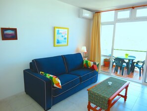 A room with a blue sofa, a small table, a picture on the wall, and a window with curtains.