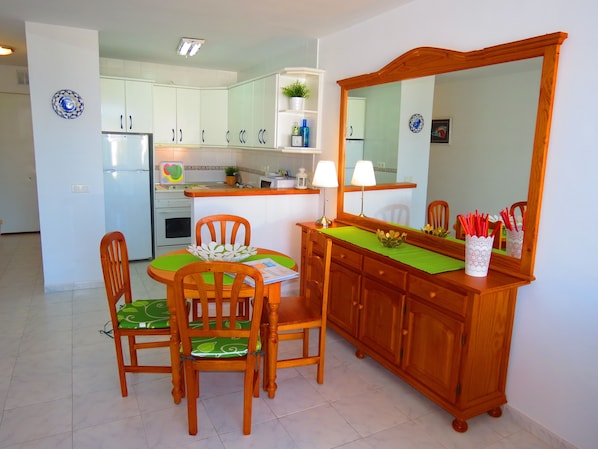 Cocina compacta con armarios blancos, una mesa de comedor con sillas, un espejo y una mesita auxiliar con un florero.