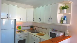 Cocina compacta con armarios blancos, lavadora, microondas y encimera de madera.