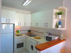 A compact kitchen with white cabinets, a washing machine, a microwave, and a wooden countertop.