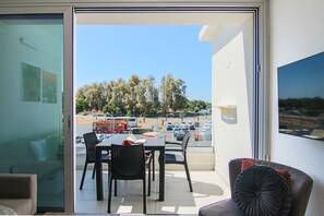 Een balkon met een tafel en stoelen, een bank en uitzicht op een parkeerplaats en bomen.