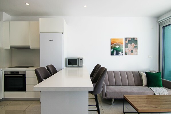 A modern kitchen with white cabinets, a microwave, and a dining area with a table and chairs.