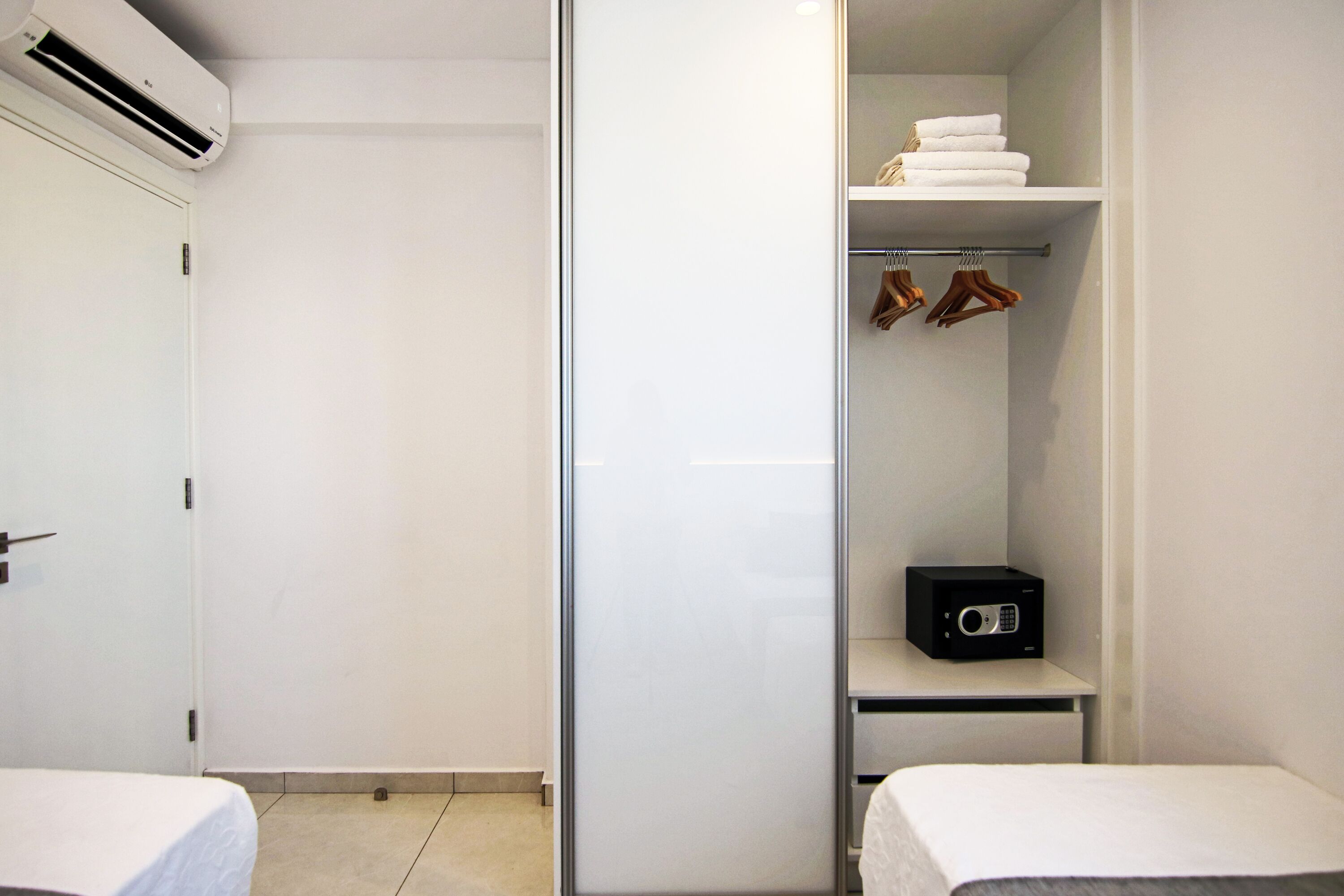 A hotel room with a bed, a closet with hanging clothes, a shelf with towels, and a microwave.