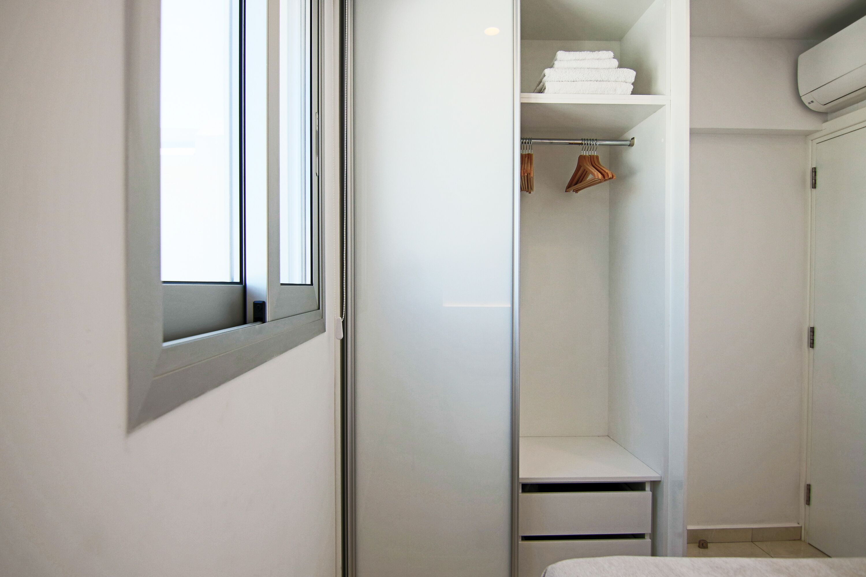 A modern, white closet with shelves, a hanging rod, and a door.