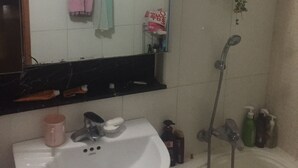 Ein Badezimmer mit weißem Waschbecken, einem Spiegel, einem Handtuchhalter mit pinken und türkisfarbenen Handtüchern, einer Dusche und einer Topfpflanze.